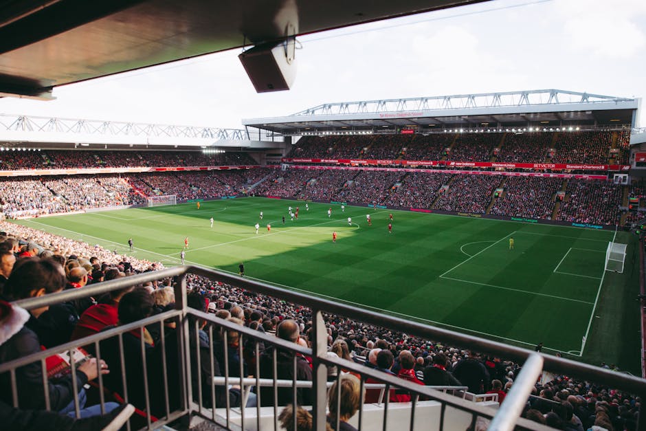 Inside Twickenham Stadium during a home football match, the view shows a well-maintained grass pitch with white boundary lines and goalposts at each end, surrounded by tiered seating filled with spect